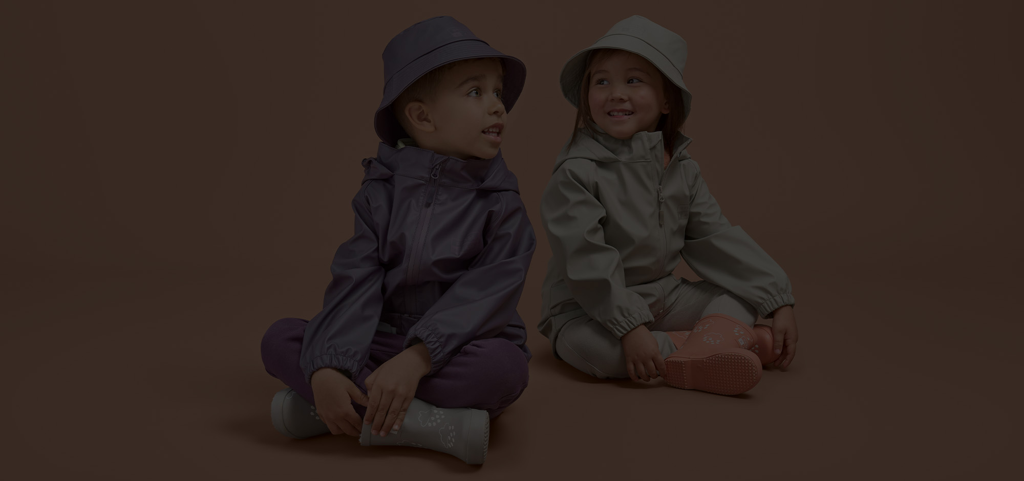 Children sat down wearing rainwear & wellies